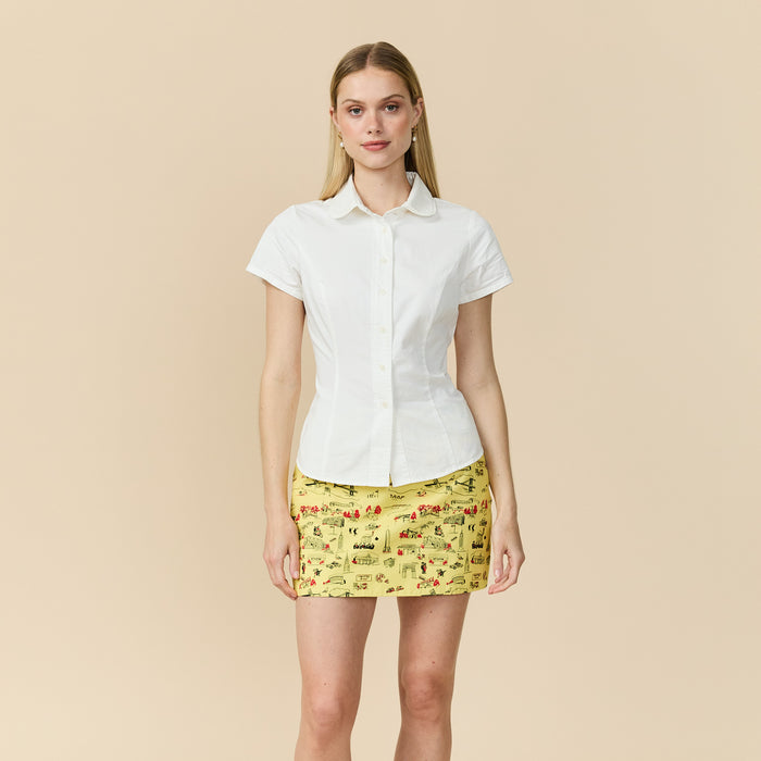 Woman wearing a white shirt and yellow patterned skirt on a beige background