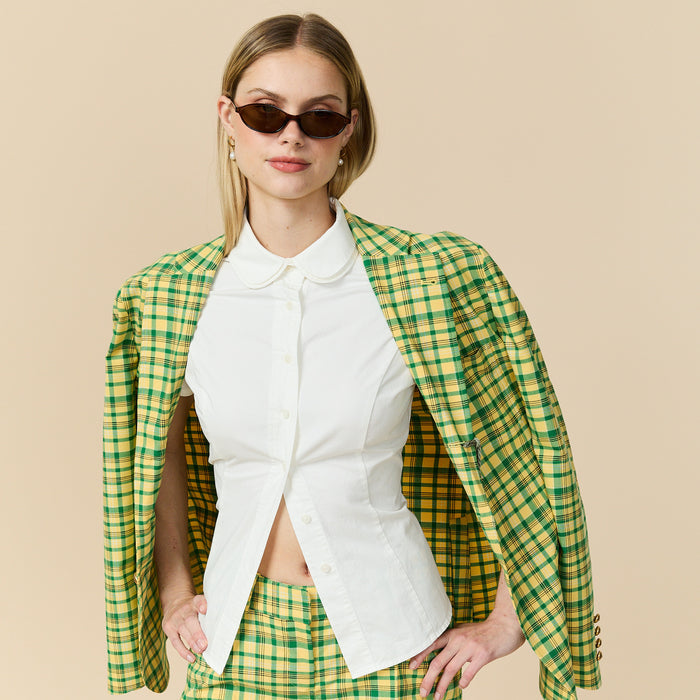 Woman wearing a green and yellow checkered jacket over a white shirt on a beige background