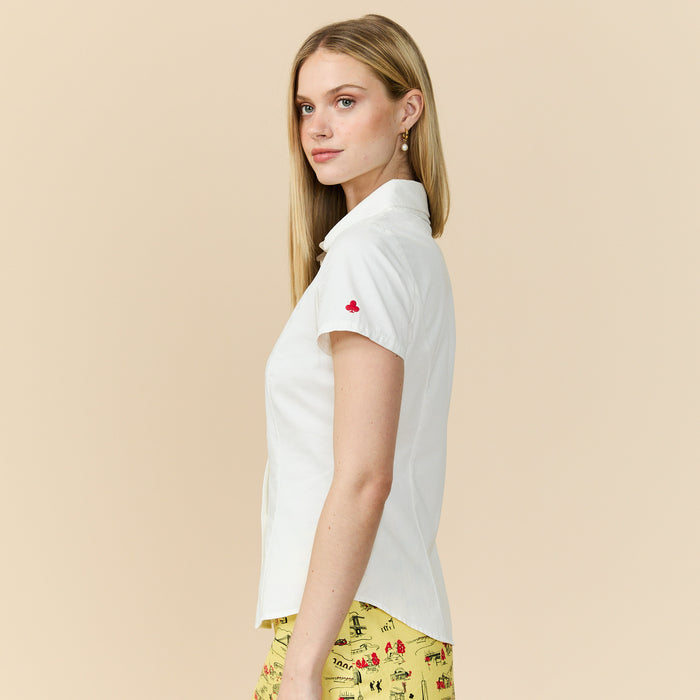 Woman wearing a white collared shirt with a red club on a beige background